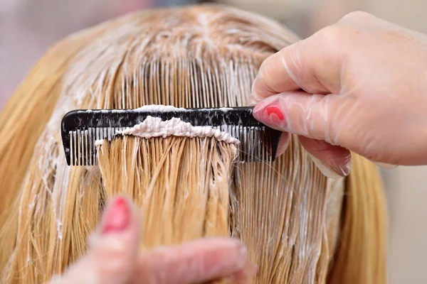 O cabeleireiro mancha a tinta em seu cabelo com um pente, para co — Fotografia de Stock