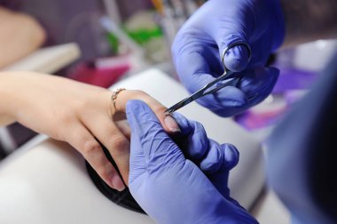 Özel bir makasla manikürcü tırnak derisini yüzüyor.