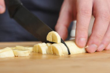 Adam tahtada büyük bir bıçakla muz dilimliyor.