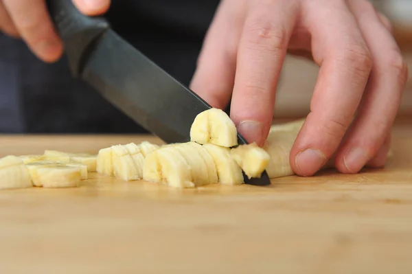Man slices a banana with a large knife on a wooden board