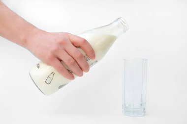 Bir adamın eli şişeden bardağa süt döker. Beyaz arkaplanda yakın plan