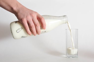 Bir adamın eli şişeden bardağa süt döker. Beyaz arkaplanda yakın plan