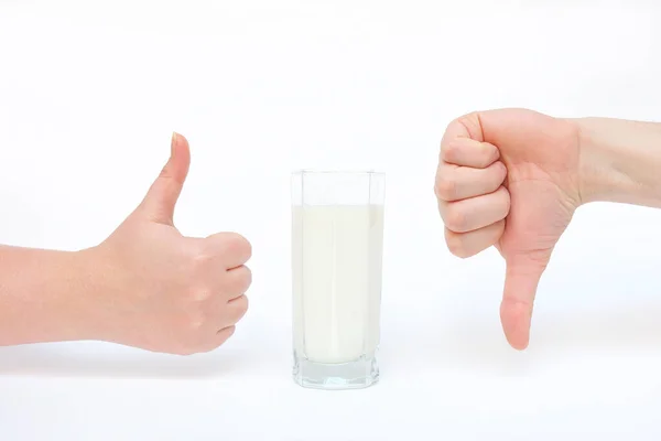 Egy pohár tej és kéz közelkép egy jelet mutat - tetszik és nem tetszik. A tej hasznos és nem hasznos, káros és nem ártalmas — Stock Fotó