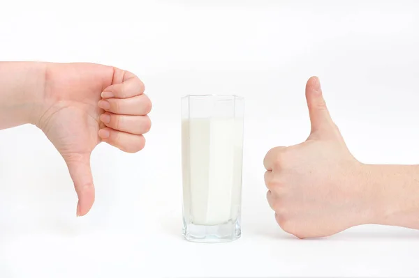Egy pohár tej és kéz közelkép egy jelet mutat - tetszik és nem tetszik. A tej hasznos és nem hasznos, káros és nem ártalmas — Stock Fotó