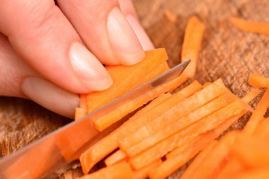 Havuç kesme. Bıçaklı kadın eller kesme tahtasındaki havuçları doğruyor. Yakın plan.