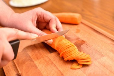 Havuç kesme. Bıçaklı kadın eller kesme tahtasındaki havuçları doğruyor. Yakın plan.