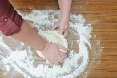 Kadınların elleri mutfaktaki hamuru masanın üzerinde yoğurur. Yakın plan.
