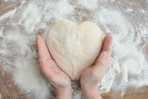 Raw dough in the shape of a heart and a touch of hands to it. Hands gently touch the raw dough in the form of heart. Close-up