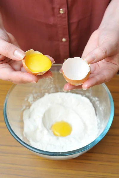 A női kezek elválasztják a tojásfehérjét a sárgájától egy tál búzaliszt felett a konyhában. — Stock Fotó
