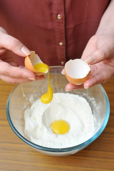 Female hands separate the egg white from the yolk over a bowl of wheat flour in the kitchen — Stock Photo, Image