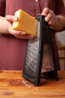 Ev mutfağında makarna pişirmek için rendelenmiş peynir doğrayan kadınların elleri. Yakın plan.