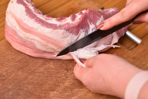 La donna taglia il grasso sulla carne cruda. Tagliare il grasso in eccesso dalla carne di maiale sulle costole. Rimuovere il grasso indesiderato sulla carne — Foto Stock