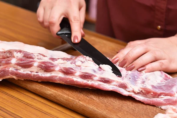 Frau schneidet Fett auf rohem Fleisch. Überschüssiges Fett aus Schweinefleisch auf die Rippen schneiden. um unerwünschte Fette auf dem Fleisch zu entfernen — Stockfoto