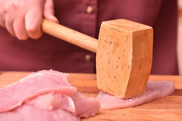 Cooking turkey meat, chops. Women\'s hands using a special wooden hammer soften turkey meat before cooking. Close-up