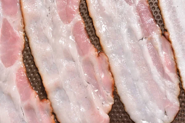 Il bacon viene fritto in una padella con un rivestimento antiaderente. Primo piano. Strisce di pancetta o di lamponi cotti in padella . — Foto Stock