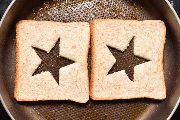 Tostadas de pan tostado con un centro en forma de estrella para crear un sándwich. El pan se fríe para sándwiches en una sartén con un recubrimiento antiadherente, primer plano — Foto de Stock
