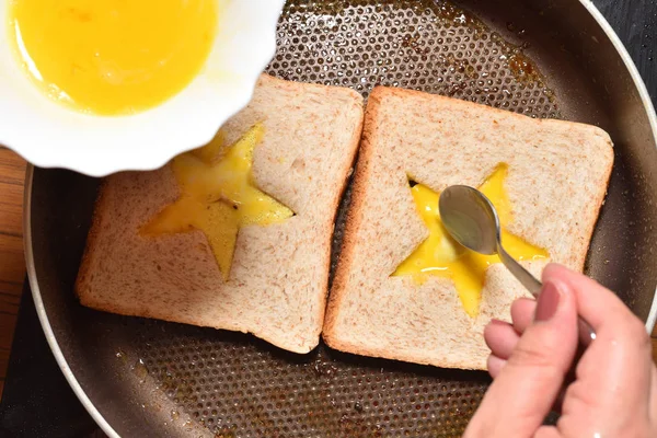 Asar pan tostado con un medio en forma de estrella y la mano de una chica lo llena con un huevo batido para crear un sándwich. El pan se fríe para sándwiches en una sartén con un recubrimiento antiadherente, primer plano — Foto de Stock