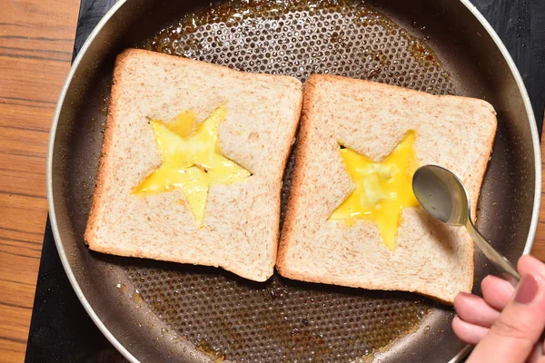 Pečení chleba toasty s hvězdou ve tvaru středu a dívčí ruka ji naplní šlehané vejce vytvořit sendvič. Chléb je smažený na sendviče v pánvi s nepřilnavým povlakem, detailní záběr — Stock fotografie