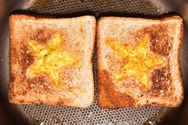 Tostadas de pan tostado con un medio en forma de estrella y tortilla llena de huevo para crear un sándwich. El pan se fríe para sándwiches en una sartén con un recubrimiento antiadherente, primer plano — Foto de Stock