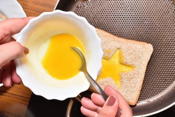 Asar pan tostado con un medio en forma de estrella y la mano de una chica lo llena con un huevo batido para crear un sándwich. El pan se fríe para sándwiches en una sartén con un recubrimiento antiadherente, primer plano — Foto de Stock