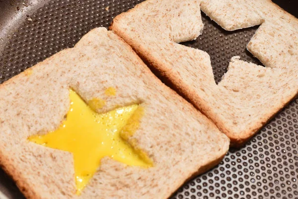 Ψητό ψωμί φρυγανιές με ένα αστέρι σε σχήμα μέση και ομελέτα γεμάτη με αυγό για να δημιουργήσετε ένα σάντουιτς. Ψωμί τηγανίζεται για σάντουιτς σε ένα τηγάνι με αντικολλητική επικάλυψη, close-up — Φωτογραφία Αρχείου