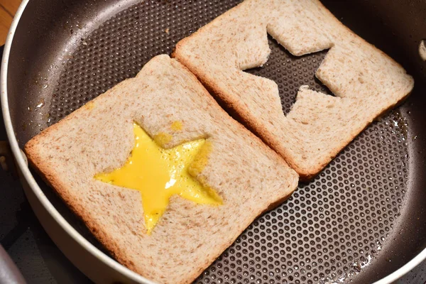 Assar torradas de pão com um meio em forma de estrela e omelete cheio de ovo para criar um sanduíche. Pão é frito para sanduíches em uma panela com um revestimento antiaderente, close-up — Fotografia de Stock