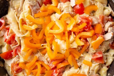 Evde makarna pişirmek. Tavada makarna ve dolmalık biberlere malzeme eklemek. Yakın plan.