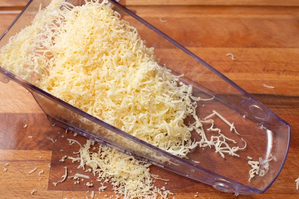 Queso rallado en un tazón transparente sobre un fondo de tabla de madera. Primer plano — Foto de Stock