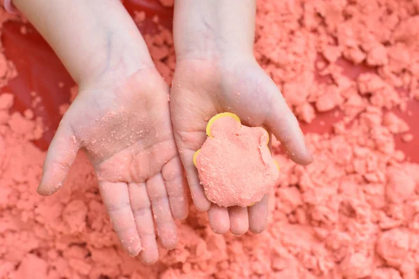 子供はピンクの運動砂でフィギュアを彫刻し、フィギュアで彼の手を示しています。トップビュー、手を閉じて — ストック写真