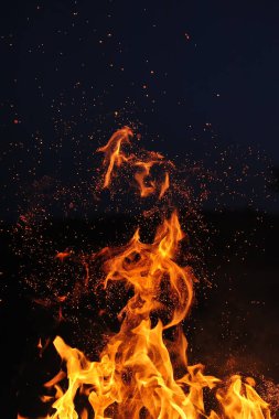 Koyu mavi gökyüzüne karşı kıvılcımlar saçan yanan bir kamp ateşinin alevi.