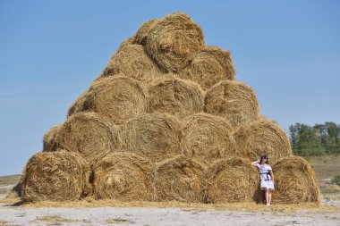 Genç bir esmer kız büyük bir saman yığınının yanında piramit şeklinde serilmişti.