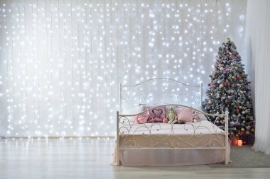 Beyaz bir duvarın arkasında soğuk çelenkler, sahte bir yatak ve bir Noel ağacı var. Tüm duvarda çelenk var, mesaj için yer var.