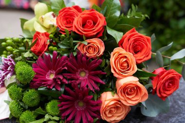 Masanın üzerinde bir buket taze çiçek var. Bir buket yeşil gül, pembe kasımpatı, anturyum, okaliptüs, falaenopsis ve şam fıstığı yeşili.