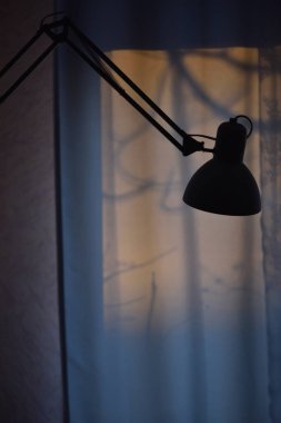 Bir masa lambasının silüeti sabahın köründe pencerenin arka planında, sabaha kadar çalışır.
