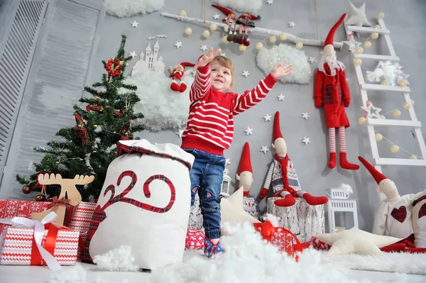 Kırmızı kazaklı küçük kız bir çantadan yapay karı alır ve onu Noel 'in arka planına cüceler, merdiven ve çelenklerle fırlatır.