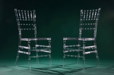 Two transparent plastic chairs on green background in photo studio with light. clipart