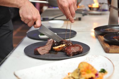 Aşçı ateşte pişmiş et parçalarını güzelce tabağa koymak için kesiyor. Yemek şovu..