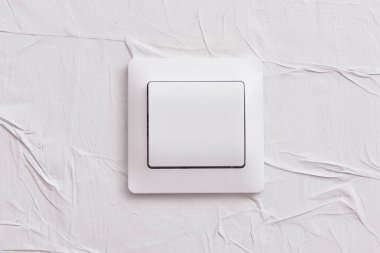 Duvarda sıra dışı sıkıştırılmış duvar kağıdı olan beyaz ışık düğmesi..