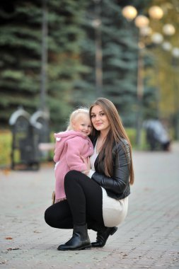 Genç anne, sonbahar parkında yürürken tatlı sarışın kızına sarılıyor..