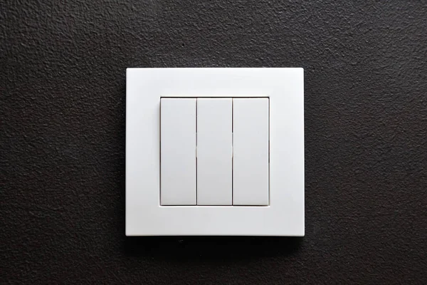Triple wall light switch on black wall.