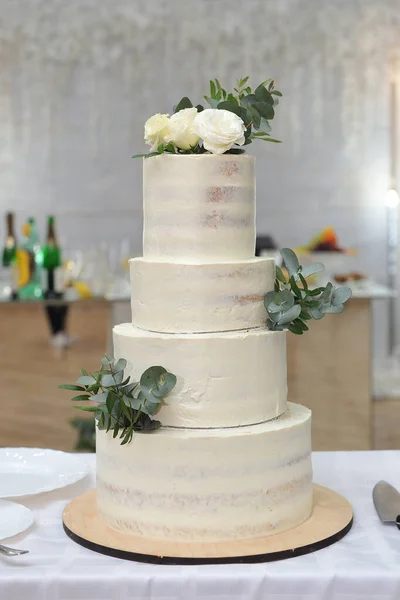 Four-tiered wedding cake decorated with cream, eucalyptus twigs and rose flowers.