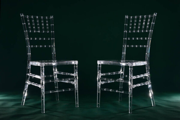 Two transparent plastic chairs on green background in photo studio with light.