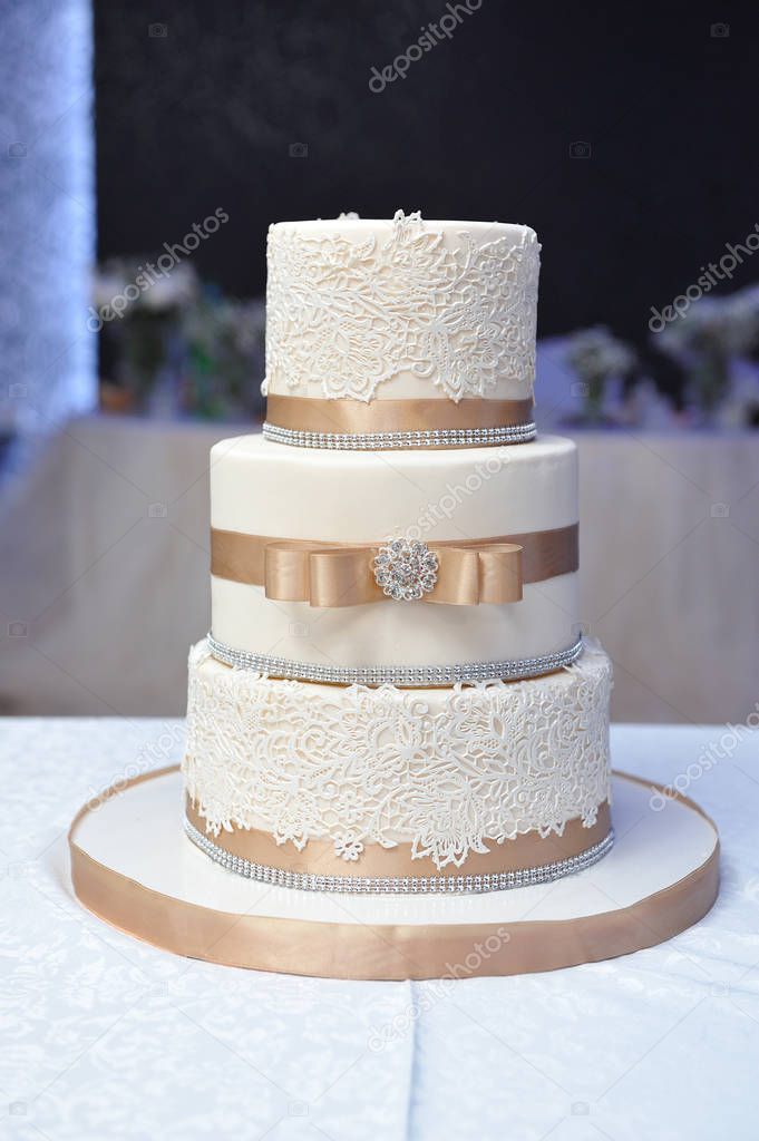 Three-tiered wedding cake decorated with mastic and beige ribbons.
