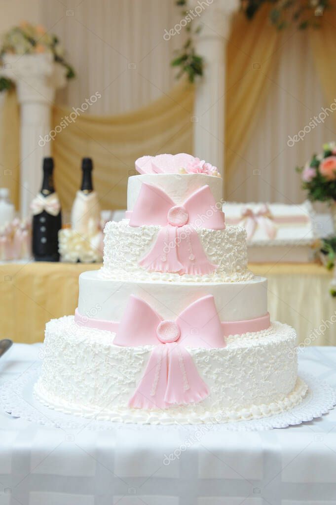 Four-tiered cake decorated with white cream and pink mastic ribbons.