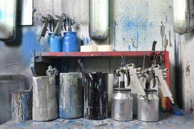Boya odasındaki masa boyayla boyandı. Masanın üzerinde su ve boya dolu sprey tabancalar ve kaplar var. Boya odası ve fabrika atölyesi
