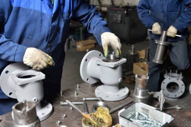 The base for the valve mounted on iron table for assembly at the factory and the worker installing and fastening the components. Close up clipart