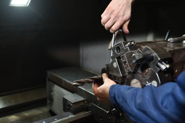 Cnc makine aracının makine metal parçası için mavi iş giysisi matkabı yükleme işçisi. İşçinin elleri yakın çekimde, Cnc kulesine matkap yerleştiriliyor