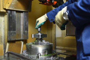 İşçi, Cnc makinesini işlemek için yeni metal parçaları yüklüyor. İşçinin elleri makineyi kapatıyor, bağlıyor ve işlemek için detay oluşturuyor.