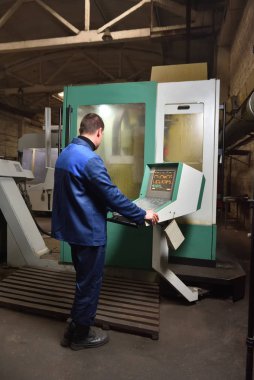 Mavi iş elbisesi işçisi, Cnc makinesini çalıştırıyor, süreci denetliyor. Cnc makinesiyle fabrikada çalışan adam..