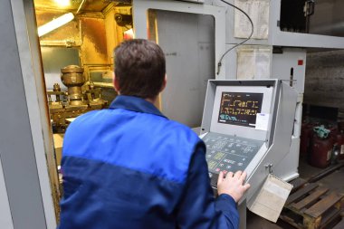 Mavi iş elbisesi işçisi, Cnc makinesini çalıştırıyor, süreci denetliyor. Cnc makinesiyle fabrikada çalışan adam..
